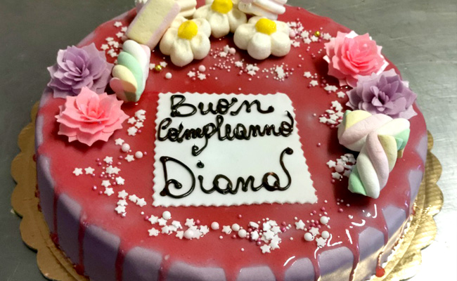 Torta ricoperta in pasta di zucchero con glassa alla fragola e decorata con fiori e marshmallow