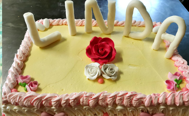 Torta con pan di Spagna, crema Chantilly e fragole, decorata sui toni del rosa con rose di zucchero e scritta in 3D.